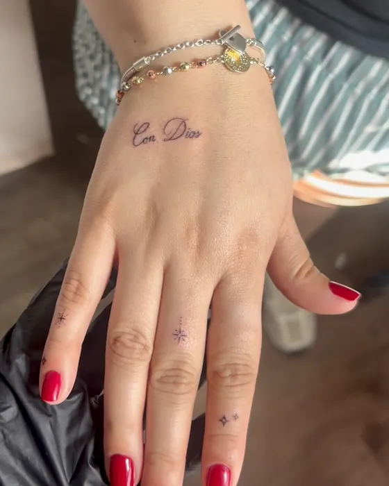 Small script reading Con Dios on the hand, with tiny sparkles on the fingers