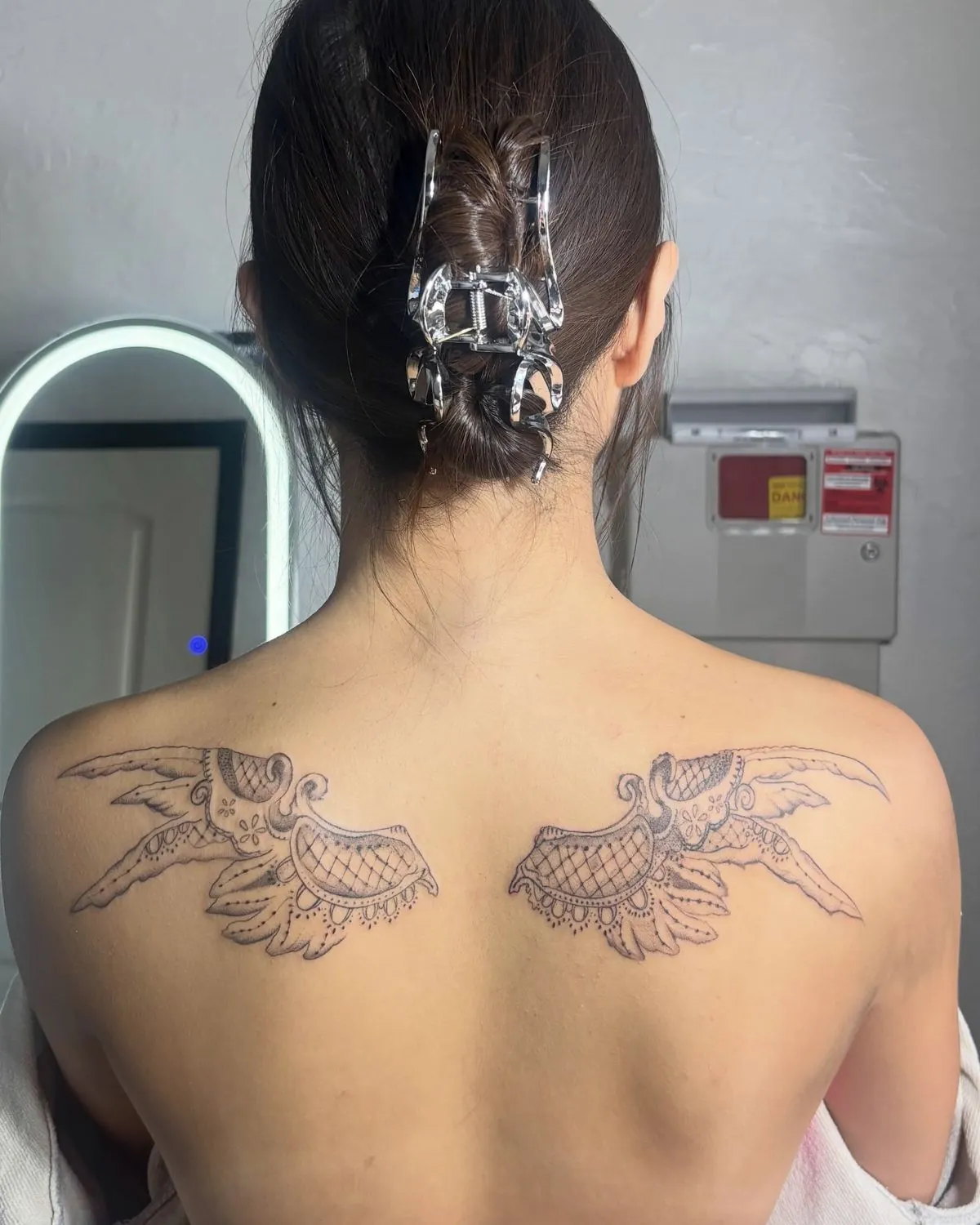 Matching fine line angel wing tattoos across a client's upper back