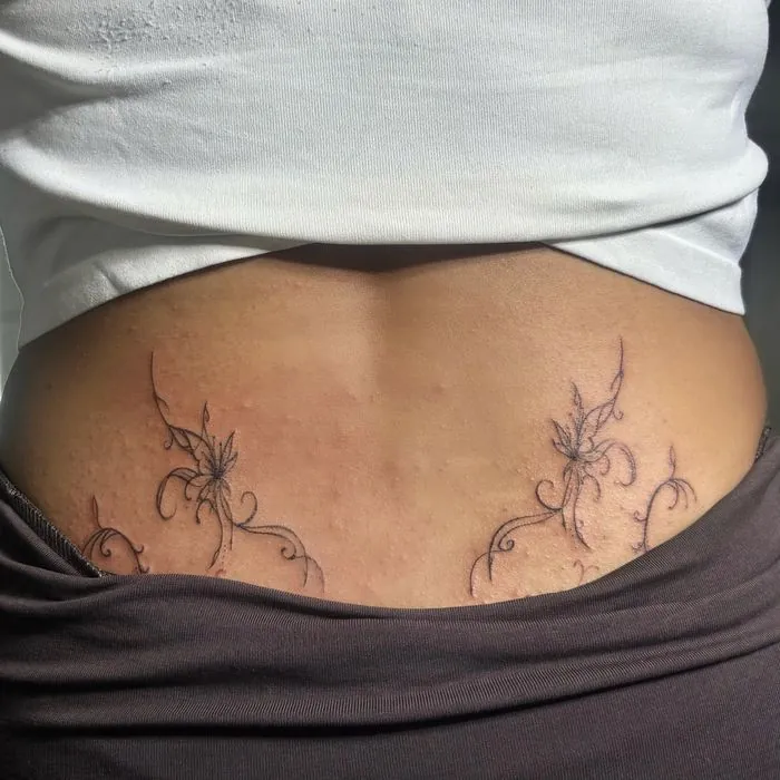 Delicate fine line floral vines across the lower back. View on Instagram.