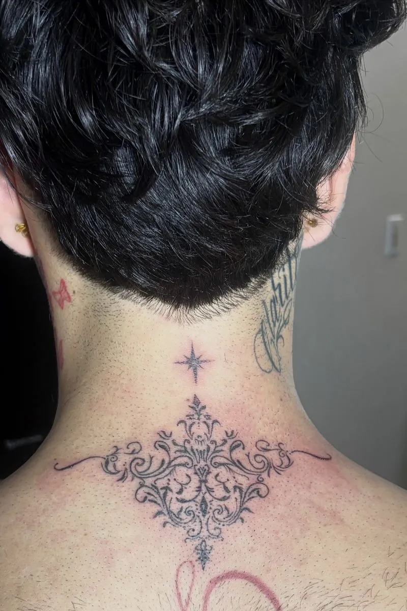 Ornamental filigree tattoo at the base of the neck, with a small sparkle above